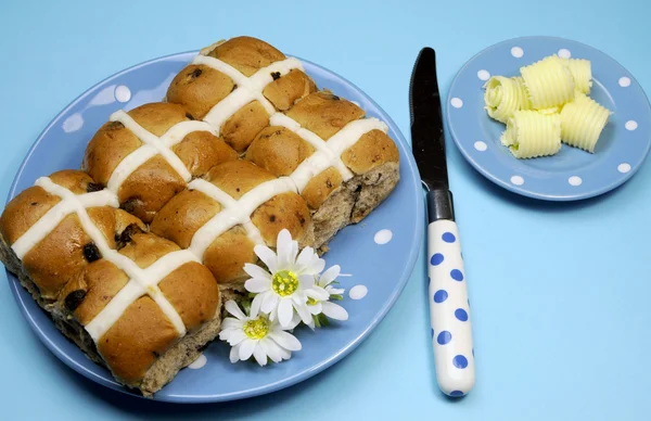 Traditionele Australische en Nederlands goede vrijdag maaltijd, hot cross broodjes, op blauwe polka dot plaat met mes en boter krullen op blauwe achtergrond. — Stockfoto