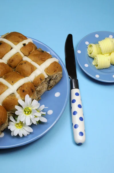 Traditionele Australische en Nederlands goede vrijdag maaltijd, hot cross broodjes, op blauwe polka dot plaat met mes en boter krullen op blauwe achtergrond. verticale antenne oriëntatie. — Stockfoto