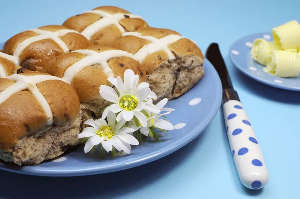 Tradizionale pasto del Venerdì Santo australiano e inglese, Hot Cross Buns, su piatto a pois blu con riccioli di coltello e burro su sfondo blu. Primo piano . — Foto Stock