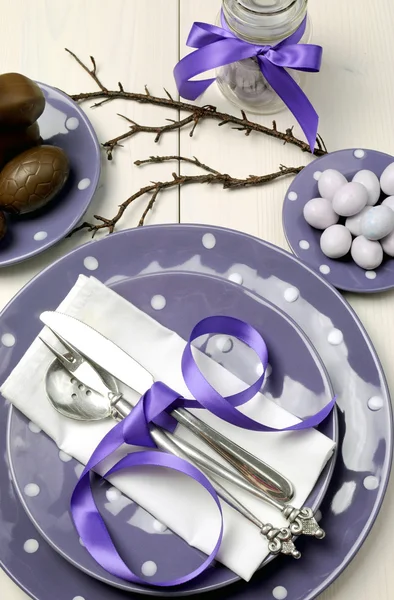 Purple theme Easter dinner, breakfast or brunch table setting with chocolate bunny rabbit, and sugar candy coated birds nest eggs on polka dot plates on white shabby chic natural wood table. — Stock Photo, Image