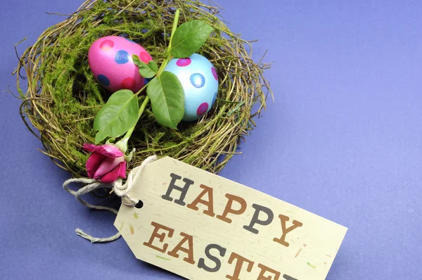 Rosa und blau gepunktete Eier mit Rosenknospe im Nest mit fröhlichem Ostergeschenk-Anhänger. — Stockfoto