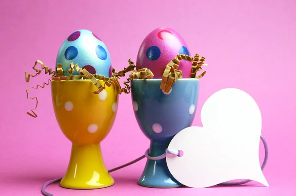 Rosa und blaue Ostereier in gepunkteten Eierbechern mit weißem Herz Geschenkanhänger — Stockfoto
