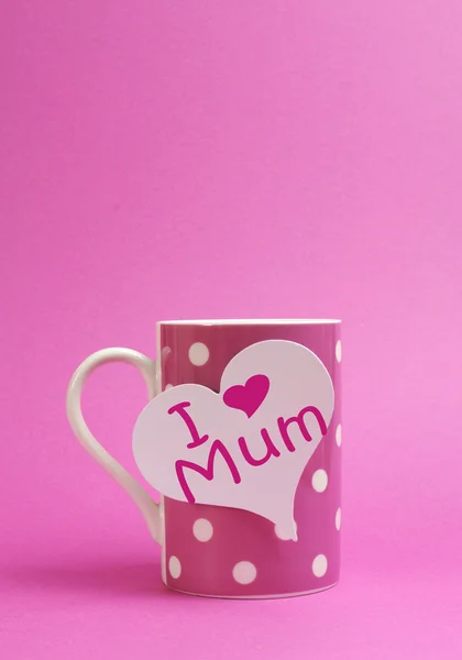 Pink polka dot coffee or tea mug with heart shape white gift tag with I Heart Love Mum for Mothers Day on pink background with copy space for your text here.