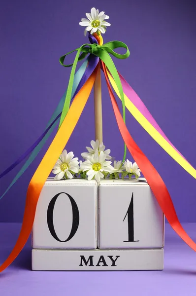 Dzień maja, 1 maja, biały blok kalendarza odarty i tęczy kolor wstążkami i kwiatami na tle fioletowy. — Zdjęcie stockowe