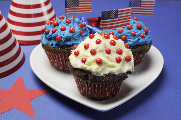 Fourth 4th of July party celebration with red, white and blue chocolate cupcakes on white heart plate and USA American flags - closeup.