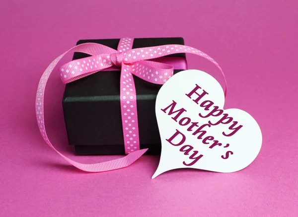 Special small black box present gift with pink polka dot ribbon and white heart shape gift tag with for Mothers Day, with message. — Stock Photo, Image