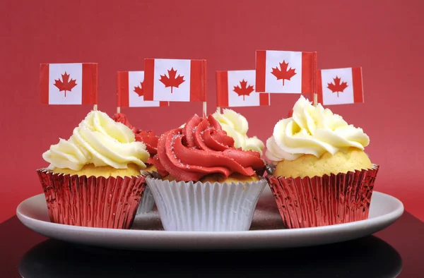 Cupcake rossi e bianchi con bandiere nazionali in foglia d'acero canadese su uno sfondo rosso per la Giornata del Canada o le festività nazionali canadesi . — Foto Stock