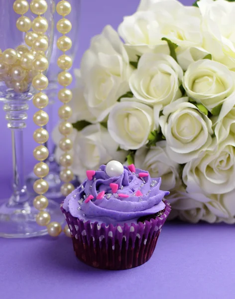 Bruiloft boeket van witte rozen met paarse cupcake en parels in champagne glas, tegen paarse Lila achtergrond. verticale close-up — Stockfoto