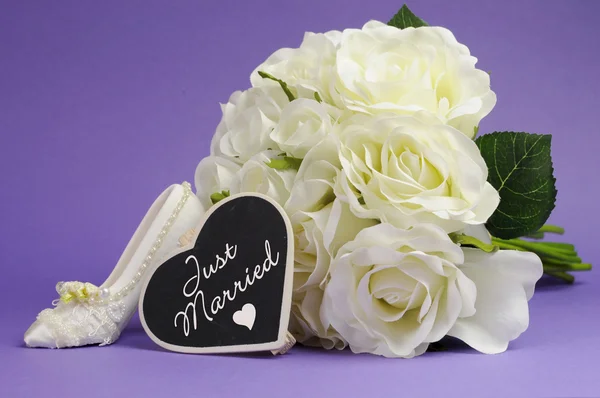 Wedding bouquet of white roses with good luck high heel shoe and heart sign with Just Married message, against purple lilac background. — Stock Photo, Image