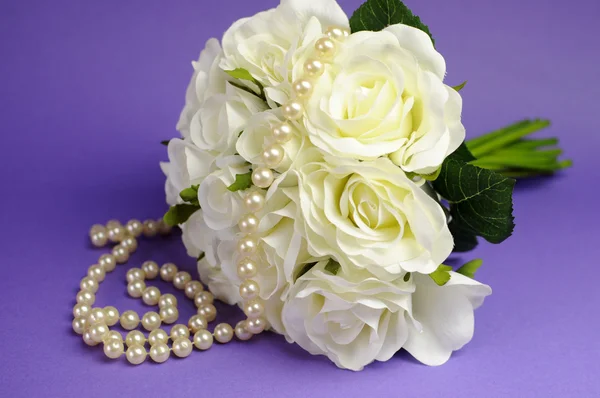 Wedding bouquet of white roses with string of pearls necklace and heart sign against purple lilac background. — Stock Photo, Image