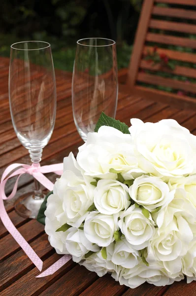 Wedding bridal bouquet of white roses with two champagne glasses with pink polka dot ribbon on outdoor garden table setting after rain. Vertical. — Stock Photo, Image