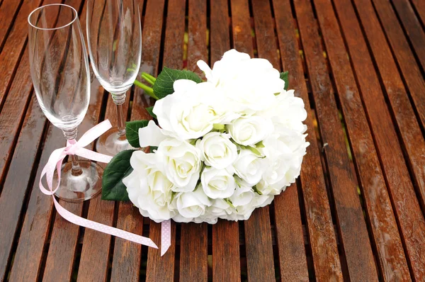 Wedding bridal bouquet of white roses with two champagne glasses with pink polka dot ribbon on outdoor garden table setting after rain. Horizontal with copy space. — Stock Photo, Image