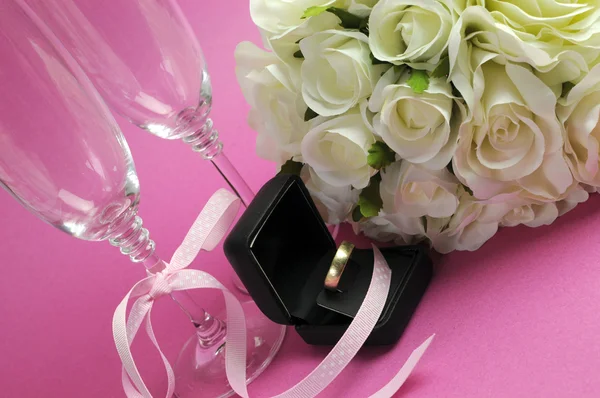 Wedding bridal bouquet of white roses on pink background with pair of champagne flute glasses and gold wedding ring in black jewelry box. — Stock Photo, Image