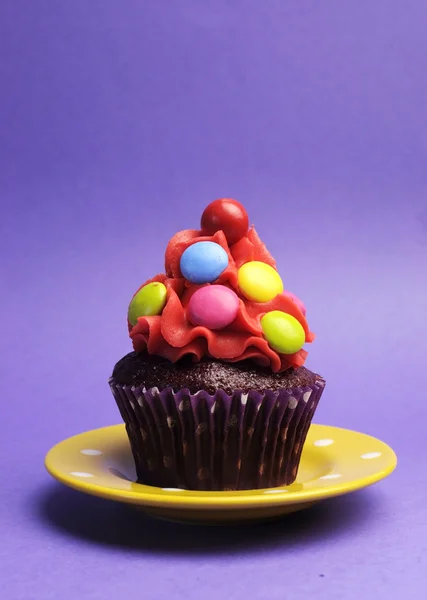 明るいキャンディ覆われた紫色の背景に黄色の水玉プレート上のカップケーキ — ストック写真