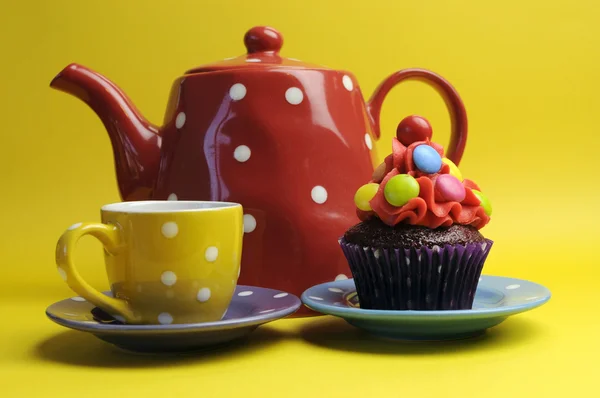 Leuchtend bunte Süßigkeiten-Cupcakes für Kindergeburtstag, Halloween oder Weihnachtsfeier vor fröhlich gelbem Hintergrund, mit roter Tupfen-Teekanne und gelber Teetasse. — Stockfoto