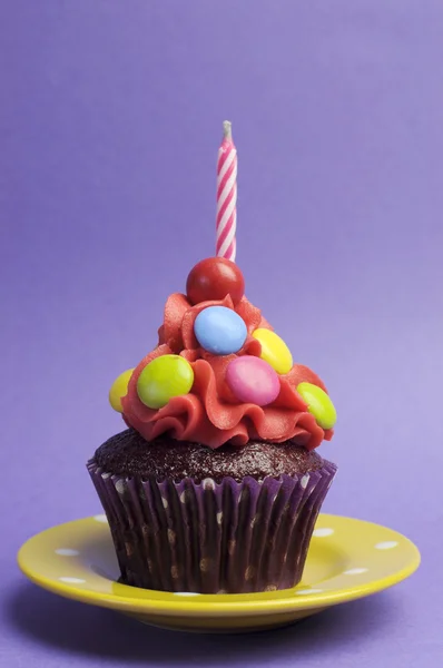 Brillante cupcake ricoperto di caramelle con candela su piatto a pois giallo su uno sfondo viola — Foto Stock