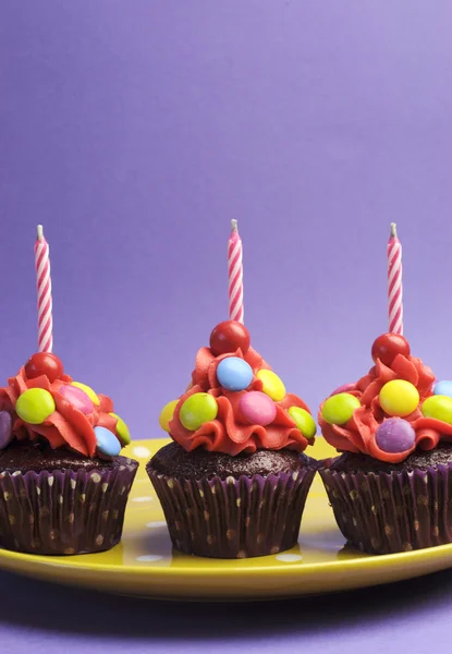 Doces brilhantes coberto cupcake na placa de bolinhas amarelas contra um fundo roxo — Fotografia de Stock