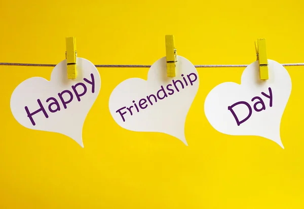 3 ホワイト ハート タグ、林にペグから掛かっている間幸せな友情日メッセージと共に国際的な友情日を祝う — ストック写真