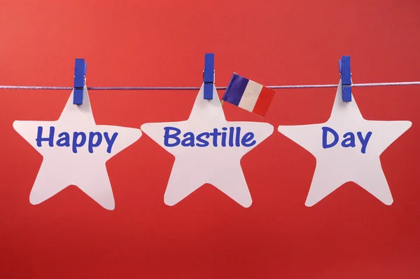 Gelukkig bastille day groet geschreven over witte sterren met een Franse vlag hangning van blauwe pinnen op een regel — Stockfoto