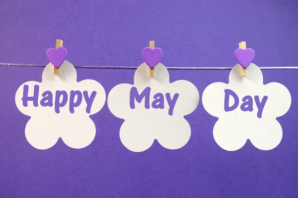Feliz mensaje de saludo del Primero de Mayo escrito a través de tarjetas de flores blancas con clavijas moradas colgando de clavijas en una línea —  Fotos de Stock