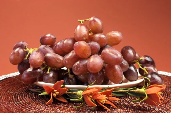 Assiette de fruits sains, raisins rouges en rouge brun automne réglage avec des fleurs . — Photo