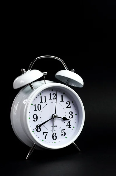 Clásico despertador blanco marcando reloj sobre fondo negro — Foto de Stock