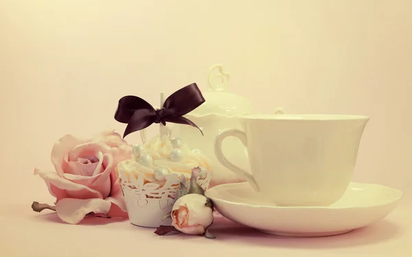 Elegant vintage retro shabby chic style afternoon or morning tea setting with cupcake and silk rose. — Stock Photo, Image