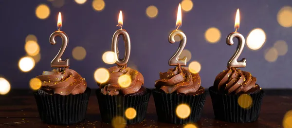 Feliz Nochevieja 2022 cupcakes de chocolate decorados con velas de oro ardiendo —  Fotos de Stock