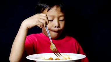 Front view, Little boy in a red shirt is eating delicious spaghetti. looks happy eating spaghetti on the black background.