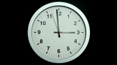 White wall clock tells the time of three o'clock. Slow rotation of the clock hands. On the black background.