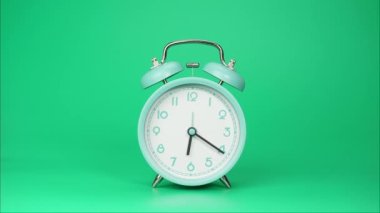 Zaman aşımı, mavi alarmlı saat zamanın akışını gösteriyor. Saatin ellerinin hareketi hızla geçti. Yeşil arka planda.