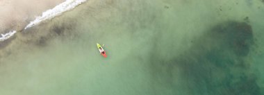 Daha aydınlık bir yaz gününde, denizde kano süren genç bir kadın, hava manzaralı insansız hava aracı.