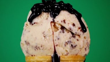 Vanilyalı çikolatalı dondurmanın üzerine çikolata sosu döküyorum. Yeşil arkaplanda yavaş akan çikolata sosu.