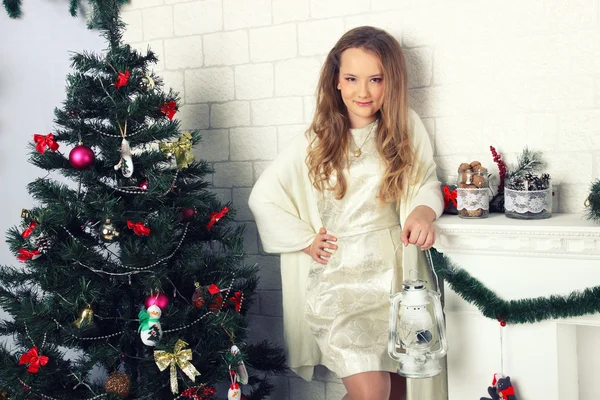 Jong meisje in een witte jurk met olielamp in de buurt van de kerstboom — Stockfoto