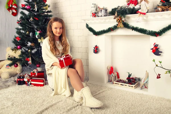 Jong meisje in een rode jurk is met gift in de buurt van de kerstboom — Stockfoto