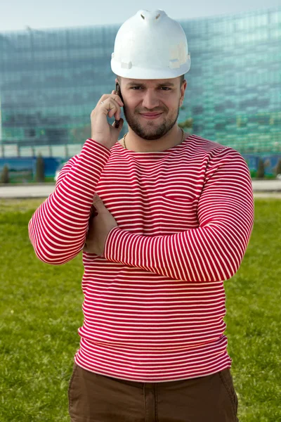 Young man in white construction helmet and red shirt using smart phone in background city