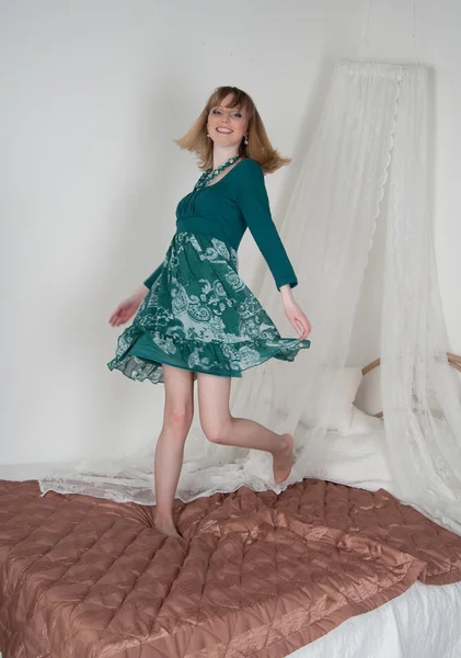 ベッドの上の緑のドレスでセクシーな女性 — ストック写真
