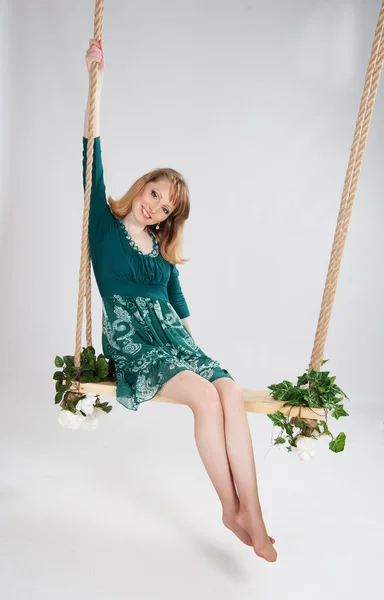 Schöne Frau in einem grünen Kleid auf einer Schaukel — Stockfoto