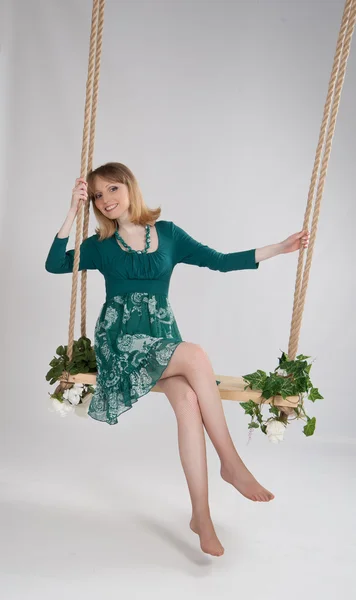 Schöne Frau in einem grünen Kleid auf einer Schaukel — Stockfoto