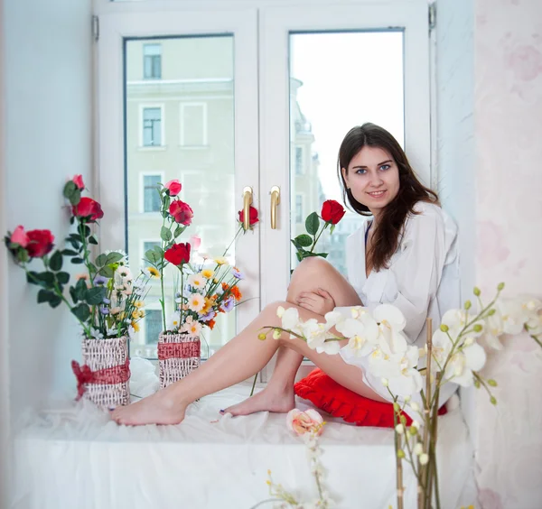 Woman in the flowers on the windowsill — Stock Photo, Image