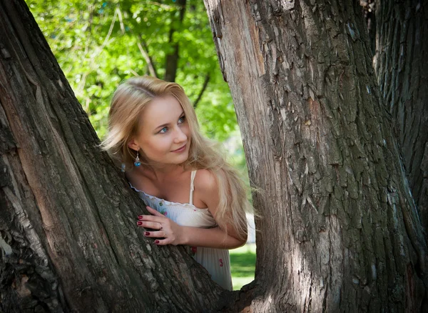 Bela, jovem mulher espreitando de trás de uma árvore — Fotografia de Stock