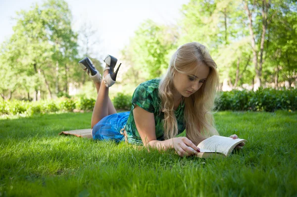 Flicka lägger på gräset med en bok — Stockfoto