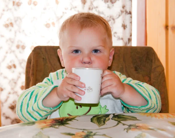 Маленький мальчик пьет за столом — стоковое фото