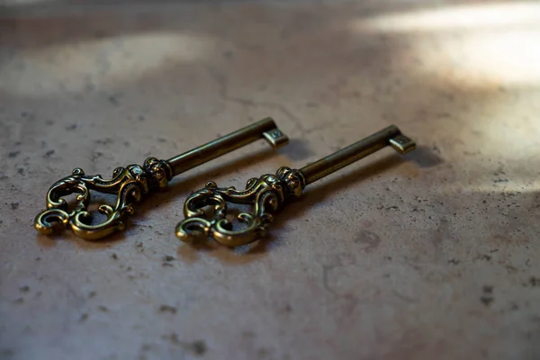 Two bronze, copper vintage keys on a stone beige background close-up