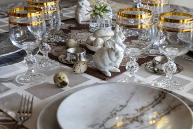 Paskalya için dekore edilmiş şölen masası. Tavşan, bıldırcın yumurtası, bardak, tabak ve sofra örtüsüyle kaplı çatal bıçak takımı. Yan görünüm