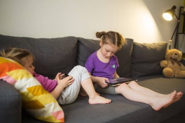 Kardeşinin çocukları evlerinde kanepede oturuyor, telefona bakıyor, video aracılığıyla iletişim kuruyor. çocuk aygıtı uygulamaları.