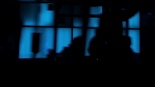 Siluetas frente a una pared de vidrio iluminado azul — Vídeo de stock
