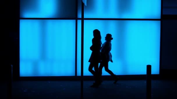 Silhouettes in front of a blue illuminated glass wall — Stock Video