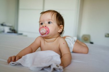 Küçük beyaz bir kız bebek, altı aylık çıplak karın üstü uzanmış, bebek bezi takmış, parlak oda fotokopi odası manzaralı.