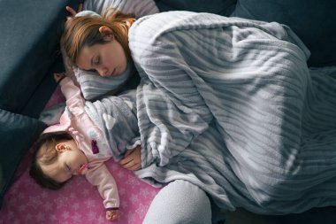 Küçük beyaz bebek kanepede annesiyle birlikte uyuyor. Bekar anne, ebeveynlikten, annelik bakımından ve bağ kurma kavramından bıkmış.